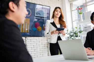 Neşeli ve kendine güvenen Asyalı bir iş kadını monitörden gelen verileri ofis arkadaşlarına göstermek için tablet kullanır. Toplantıda Asyalı kadın lider rolüne odaklan.