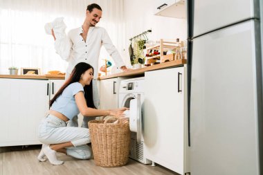 Kafkasyalı mutlu çift birlikte çamaşır yıkarken eğleniyor. Çiftler birlikte çamaşır sepetinden kirli çamaşırları evdeki çamaşır makinesine yüklemeye yardım ediyorlar. Aile haftalık angarya işler yapıyor..