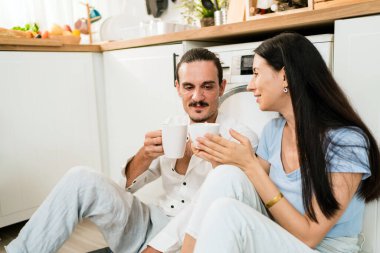 Mutfak zemininde birlikte oturup keyifli sohbetli kahve içen mutlu beyaz çift. Kadın ve erkek evdeyken konuşuyorlar. Birlikte yaşayan çift konsepti.