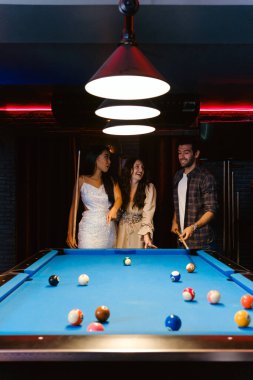 Genç çeşitlilikteki insanlar gülümseme, keyif ve eğlenceyle bilardo oynuyor. Gençler gece kulübündeki bilardo salonunda vakit geçiriyorlar. Erkekler, kadın arkadaşlar bilardo oynuyor. Gece hayatı konsepti