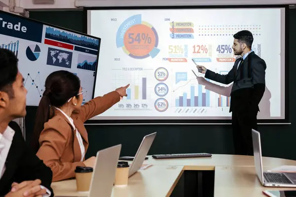 Neşeli ve kendinden emin Asyalı bir işadamı projektör ekranından gelen bilgileri ofis arkadaşlarına sunuyor. Toplantıda Asyalı işadamı rolü.