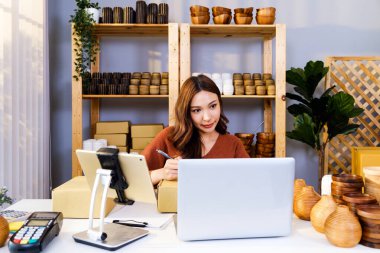 Asyalı güzel kadın evde canlı yayın yapan vazo ürünleri satıyor. Çekici genç bir kız paketin üzerine göndermek için müşterinin adresini yazar. Uzak satın alma ve satın alma kavramı.