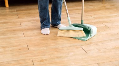 Evde çalışan genç, profesyonel bir temizlikçi kadın görüntüsü. Hizmetçi kızlar süpürgeleri ahşap zemine süpürür ve kanepenin altını temizler. Temizleyici ve angarya konsept