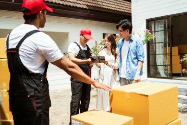 Birkaç kişi, üniformalı Asyalı ve Kafkasyalı işçilerin karton kutuları boşalttıkları listeyi imzaladı. Teslimatçılar çiftler için kutuları boşaltıyor. Profesyonel dağıtım ve taşıma hizmeti.