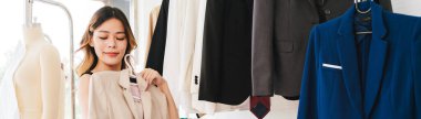 Bir kadın moda mağazasında giysi eşyasıyla poz veriyor, çeşitli renkli giysiler sergileniyor..