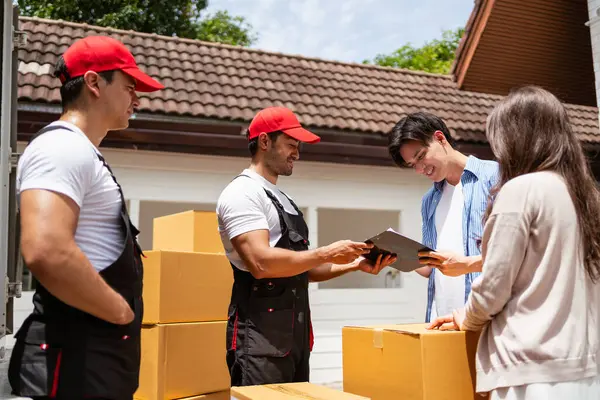 Birkaç kişi, üniformalı Asyalı ve Kafkasyalı işçilerin karton kutuları boşalttıkları listeyi imzaladı. Teslimatçılar çiftler için kutuları boşaltıyor. Profesyonel dağıtım ve taşıma hizmeti.