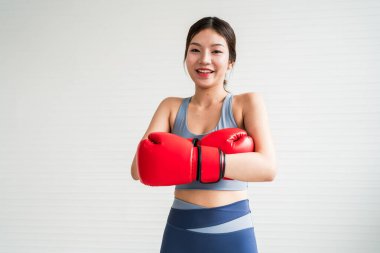 Gülümseyen bir kadın kırmızı boks eldiveni ve spor kıyafeti giyiyor, eğitime hazır, parlak bir çevrede enerji ve kendine güven göstermeye hazır..