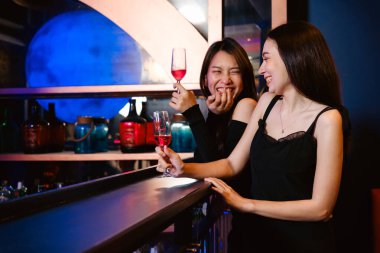 İki kadın neşeyle bardakları tokuşturur canlı bir barda, renkli ışıklar altında içkinin ve kahkahanın tadını çıkarırlar..