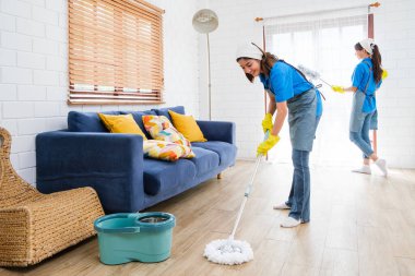 İki kadın modern bir oturma odasını temizliyor, biri yerleri paspaslarken diğeri tozlanıyor, temiz ve parlak bir atmosfer yaratıyor. Temizlik ve angarya küçük işletme konsepti