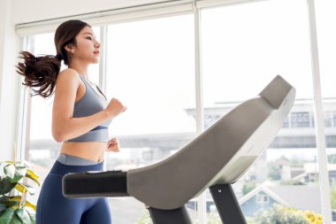 Parlak, modern bir spor salonunda koşu bandında koşan bir kadın, spor salonundaki uygunluk ve sağlığını ön plana çıkarıyor. Evde çalışma kavramı..