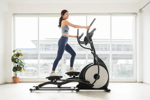 Formda bir kadın, eliptik bir makine üzerinde, parlak, modern bir kapalı alanda, sağlık ve uygunluğu teşvik ederek egzersiz yapar..