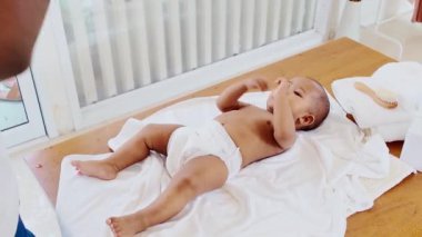 Bir bebek yumuşak bir havluya uzanır, bebek bezi giyer, neşeli ve rahat bir ortamda mutlu görünür. Neşeli bir aile anı. Mutlu çeşitlilik aile kavramı. Gerçek zamanlı 4k video.