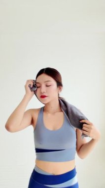 Genç bir Asyalı kadın evde egzersiz yapıyor, gülümserken havlu kullanıyor, sağlıklı bir yaşam tarzı ve formda kalma alışkanlığı sağlıyor. Evde çalışma konsepti. Gerçek zamanlı dikey 4k video