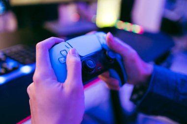 Neon ışıklı bir oyun tezgahında el ele tutuşmuş bir oyun kumandanı. Canlı ışıklandırma ve bulanık arkaplan vurgusu modern oyun, esportlar, etkileşimli eğlence.