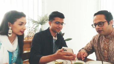 Hintli aile akıllı telefondan bir şeyler tartışırken birlikte yemek yemekten hoşlanır. Geleneksel giyimli erkek, etnik giysili kadın genç erkek, aile bağı, teknoloji, kültür gelenekleri