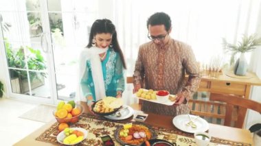 Geleneksel giyinmiş bir Hintli erkek ve kadın, güzel dekore edilmiş bir masanın üzerine şapati, naan, köri, samosa, biryani ve panipuri gibi yemekler koyarak şenlikli bir yemek hazırlıyorlar. Hint kültürü, 