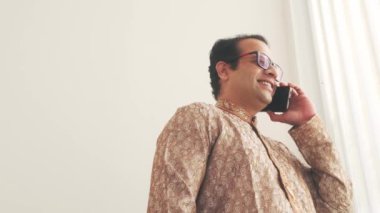 Geleneksel giyinmiş neşeli Hintli adam akıllı telefonuyla konuşuyor, sohbet sırasında gülümsüyor. Kültürel miras ve modern iletişim, bağlantı, mutluluk ve dijital bağlantının bir karışımı.