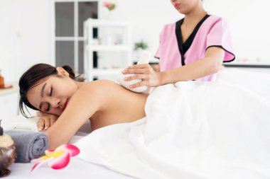 Bir kadın lüks bir kaplıcada rahatlatıcı bitkisel masajdan hoşlanır. Pembe üniformalı yetenekli bir terapist dinlenme ve kendine bakımı için dingin bir sağlık ortamında gençleştirici bir tedavi sağlar..