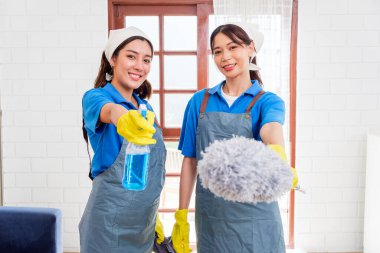 Üniformalı ve eldivenli iki profesyonel temizlikçi temizlik malzemesi tutarken gülümsüyor. Oda servisi konsepti, temizlik hizmetleri, ev temizliği, iş için profesyonel hizmetçi servisi.