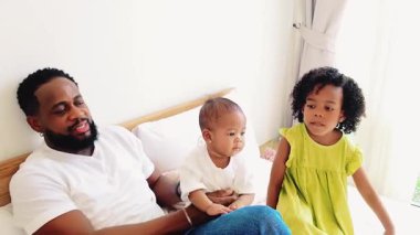 Kara Babayı sevmek, bebeği ve kızıyla rahat bir yatakta kaliteli zaman geçirmek. Aile bağları, ebeveynlik, çocukluk anları, mutluluk ve sevgiyle dolu aydınlık ev ortamları. Yavaş çekim 4k video.