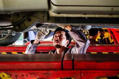 Otomobil tamirhanesinde hidrolik asansörde çalışan bir Japon tamirci. Araç bakımı, araba servisi, garaj işi, teşhis, mekanik onarım, otomotiv endüstrisi için mükemmel..
