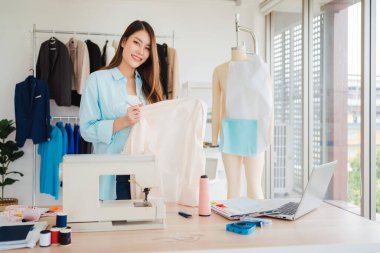 Modern bir stüdyoda çalışan yaratıcı bir moda tasarımcısı, yeni bir elbise dikiyor. Kumaşlar, aletler ve bir mankenle çevrili, işçilik, girişimcilik ve sürdürülebilir moda.