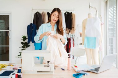 Bir moda tasarımcısı, dikiş malzemeleri, kumaş ve mankenlerle çevrili yaratıcı bir stüdyoda elbise üzerinde çalışır. Moda tasarımında zanaatkarlık, yaratıcılık ve girişimcilik..