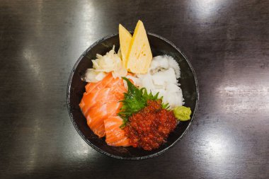 Taze somon balığı, ikura (somon yumurtası), tamago, beyaz balık ve wasabi, shiso yaprağı ve turşulu zencefil içeren canlı bir Japon kaisendonu, suşi pilavı üzerine servis edilir..