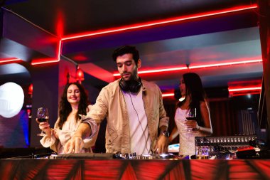Bir DJ canlı bir gece kulübünde şarkı söylerken iki şık kadın içkinin tadını çıkarıyor. Neon ışıkları, enerjik atmosfer ve müzik, canlı bir gece hayatı deneyimi için ortam hazırlar..
