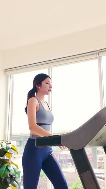 Modayı takip eden genç bir kadın parlak bir spor salonunda koşu bandında yürüyor. Y jenerasyonu ve Z jenerasyonu fitness yaşam tarzı kardiyo, sağlık, kendine bakım ve sağlık motivasyonuna odaklandı. Dikey 4k video