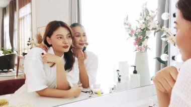 Asyalı anne ve kızı makyaj yaparken gülümseyip kaynaşırken aynı zamanda fırçalarla makyaj yapıyorlar. Anneler Günü 'nde güzellik ve aile bağını kutlamak. Yavaş çekim 4k video.