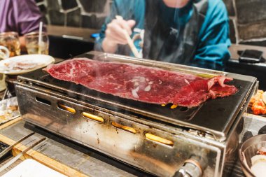 Tokyo, Japonya 'da otantik yakiniku barbekü deneyimi. İnce dilimlenmiş sığır eti, sarımsak ve soğanlı bir sıcak tabakta ızgara. Dumanlı, aromalı ve canlı Japon yemek atmosferi.