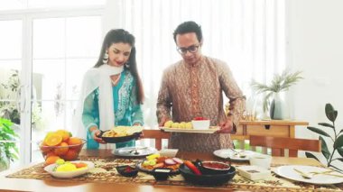 Geleneksel aile yemeği için geleneksel kıyafet sehpası olan Hintli çift, bayram yemekleri ve kültürel dekorlarla, geleneği, birlikteliği, otantik Hint mutfağını kutluyorlar. Yavaş çekim 4k video