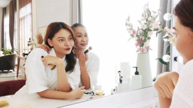 Anne ve kız makyaj zamanlarının keyfini çıkarıyorlar. Gösterişli aynanın önünde, güzel ve sıcak bir yuva ortamında kendine bakmanın tadını çıkarıyorlar. Gerçek zamanlı 4k video