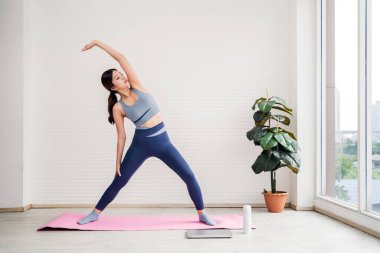 Aktivite kıyafetli genç bir kadın evde pembe yoga minderi üzerinde egzersiz yapıyor, verimliliği, sağlığını ve doğal ışık alan parlak bir mekanda kendini geliştirmeyi teşvik ediyor..