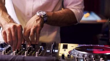 DJ 'in gece kulübünde ses karıştırıcı kontrollerini ayarlarken, şık bir saat ve beyaz gömlek giyerken, parti atmosferi, gece hayatı eğlencesi ve etkinlik kutlamaları için canlı müzikler yaratırken yakın plan görüntüleri..