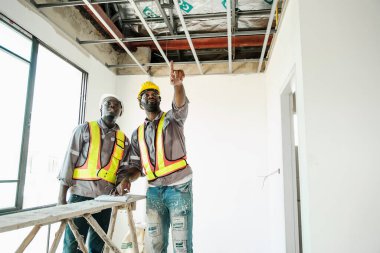 Güvenlik teçhizatlı iki inşaat işçisi iç yenileme sırasında tavanı inceliyor. Arazi denetimi, takım çalışması ve gayrimenkul geliştirmede ilerleme kavramı.