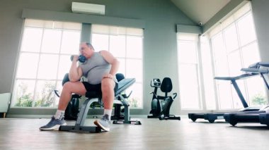 Aşırı kilolu son sınıf öğrencisi, beden eğitimi ve sağlığı için salonun dambıllarını kaldırıyor. Düzenli kas geliştirme egzersizi yoluyla sağlıklı yaşlanma, kilo kaybı ve aktif yaşam tarzını teşvik eder..