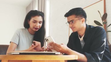 Genç Hintli iş ortakları rahat bir kafede akıllı telefonlar ve dizüstü bilgisayar kullanarak fikirleri tartışıyor. Modern takım çalışması, dijital iletişim ve mobil çalışma rahat bir ortamda.