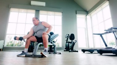 İyi ışıklandırılmış bir spor salonundaki halterin üzerinde halteri kaldıran şişman bir adam, bağlılığı, sağlıklı yaşlanmayı ve fitness 'te kişisel ilerlemeyi simgeliyor. Sağlık ve sağlık için ideal ya da kıdemli fitness temaları.