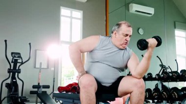 Modern bir spor salonunda halterini kaldıran kilolu son sınıf öğrencisi, güç antrenmanına odaklanıyor. Yaşlı yetişkinler için sağlıklı yaşlanma, kas geliştirme ve fitness rutinlerinde kararlılığı teşvik eder..