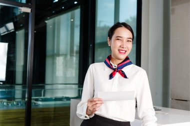 Gülümseyen kadın havayolu çalışanları gişede beklerken biniş kartı tutuyorlar. Havaalanı operasyonlarında dostane hizmet, havaalanı konukseverliği ve profesyonelliği tasvir ediyor.