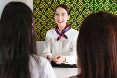 Gülümseyen havayolu çalışanları kayıt masasındaki iki kadın yolcuya belgeleri teslim ediyor. Modern havaalanında dost canlısı müşteri hizmetleri, seyahat hazırlığı ve yolcu yardımı sunar..