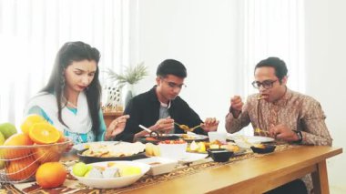 Üç kişi, Hint aile toplantılarında sohbetten ve geleneksel yemeklerden zevk alır. Kültürel çeşitliliği, toplumsal bağları ve otantik kutlamayı aydınlık bir yemek masasında vurgularlar..