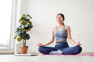 Yogadaki kadın pembe bir paspasın üzerinde huzur içinde meditasyon yapıyor, spor kıyafeti giyiyor, farkındalığı, zihinsel berraklığı, sağlık rutinini ve doğal ışıkta sakin ve sağlıklı bir yaşam tarzını temsil ediyor..