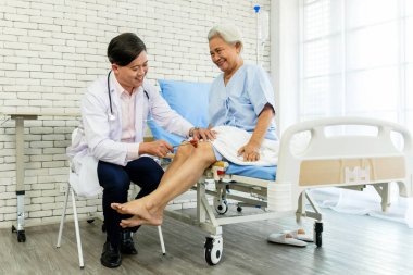 Bir doktor hastane kontrolü sırasında yaşlı bir kadının dizine refleks testi uygular. Sahne şefkatli bir bakım, tıbbi uzmanlık ve kıdemli sağlık ve sağlığın önemini gösteriyor.