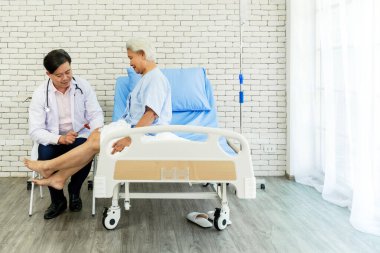 Erkek bir doktor, hastane yatağında oturan yaşlı bir kadına diz refleksi testi uygular. Sahne, profesyonel tıbbi bakım, yaşlılık sağlığı ve parlak, klinik bir ortama olan güveni vurguluyor..