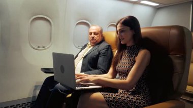 İş gezginleri uçuş sırasında bilgisayarda çalışmak için Wi-Fi kullanıyorlar. Sahne, rahat bir havayolu kabininde uçarken bağlantı, verimlilik ve dijital yaşam tarzını vurguluyor.