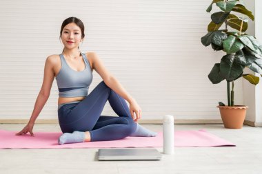 Parlak bir ev ortamında yoga minderinin üzerinde uzanan genç bir kadın farkındalık ve zindelik pratiği yapıyor. Aktif giysiler içinde sakin, esnek ve ev içi egzersizlerle sağlıklı bir yaşam sürüyor..