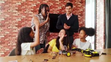 Mutlu çocuklar bir robotik sınıfında başarıyı kutluyorlar, BTMM kodlama projesini tamamladıktan sonra öğretmenlerine beşlik çakıyorlar. Eğitim teknolojisinde takım çalışması ve yenilik ruhuna sahip çeşitli gruplar.